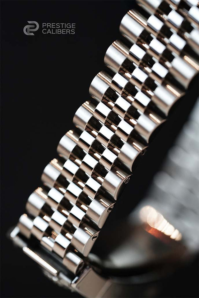 Close-up of a jubilee bracelet with 'Prestige Calibers' branding on a dark background.