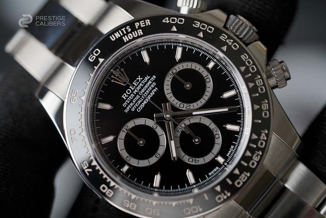 Close-up of a Rolex watch with black dial and silver case, branded 'Prestige Calibers'.